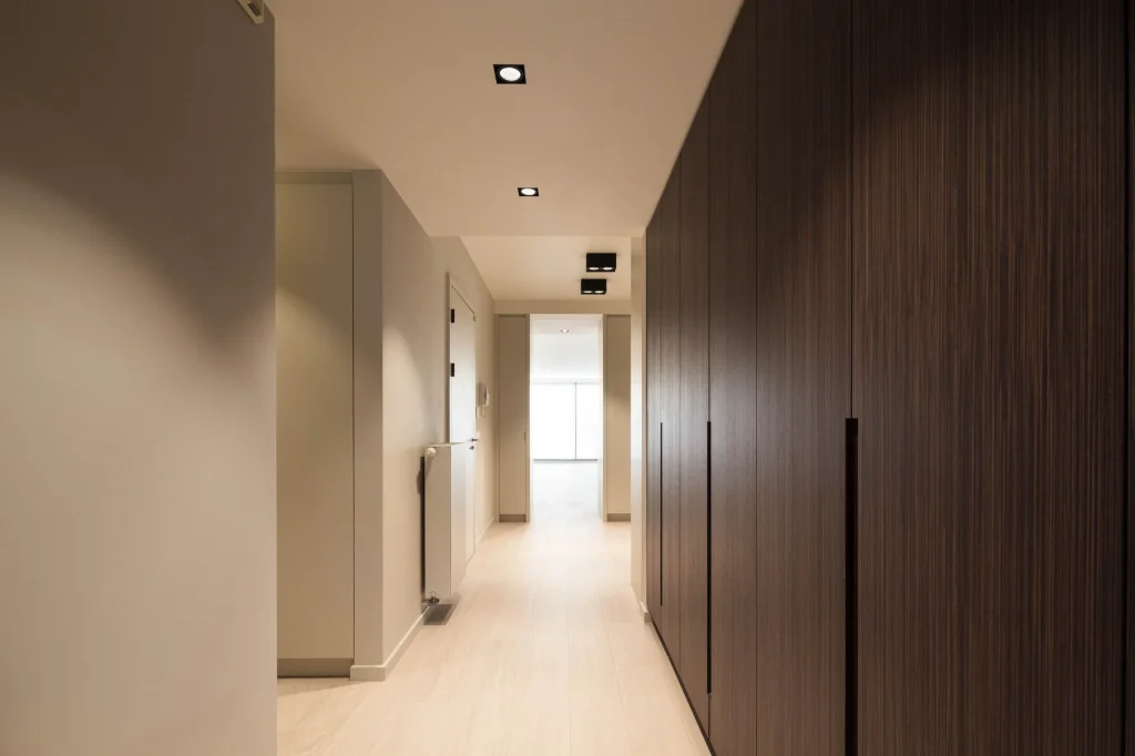 Vestiaire en bois foncé avec éclairage sur mesure dans un appartement rénové à Uccle, projet global signé Robert Vanhecke et réalisé par Renov Management